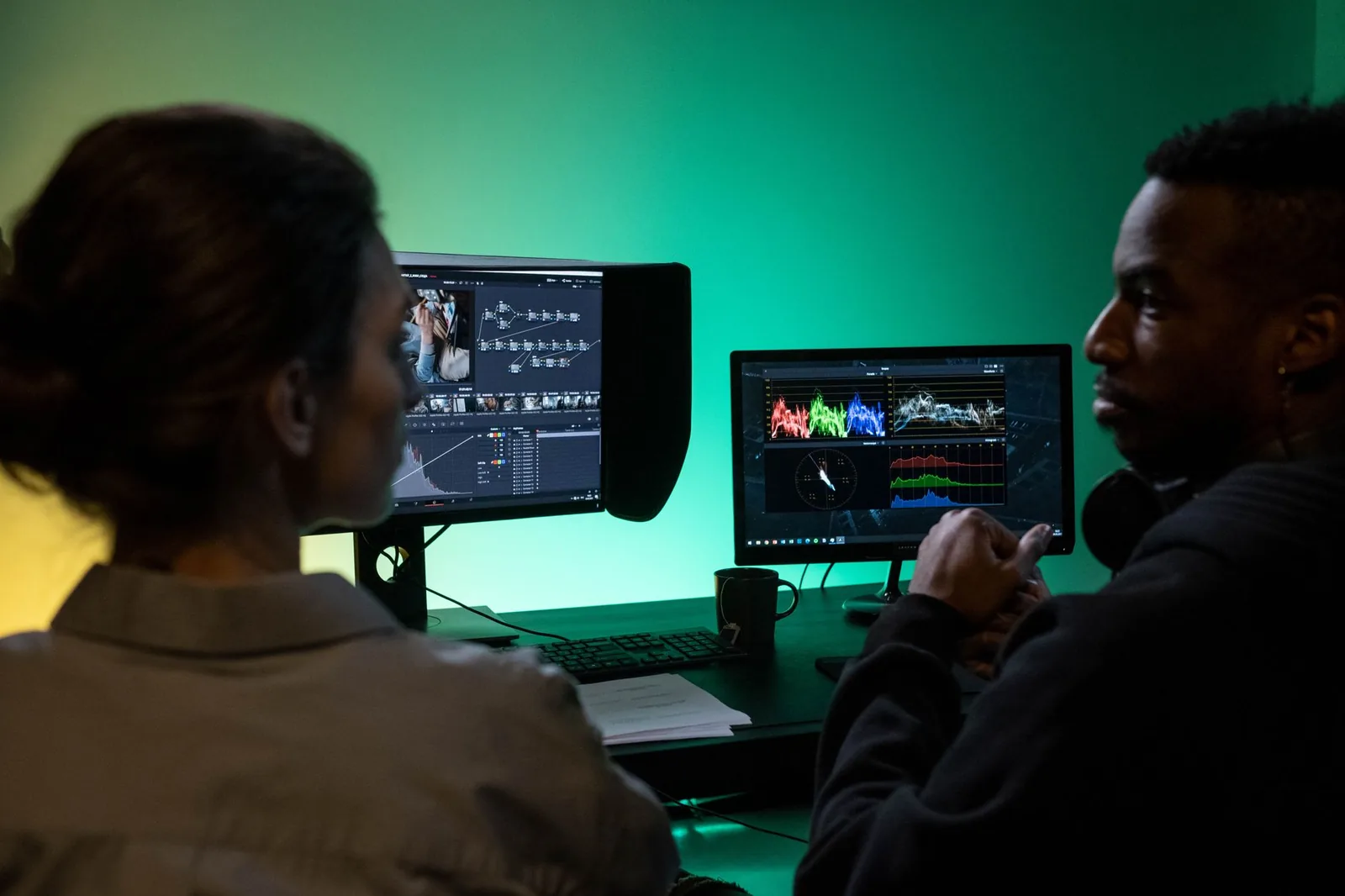 Two colleagues reviewing video edits and color grading together on dual monitors